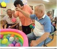 ビニールプールのボールをすくって遊ぶ利用者さま